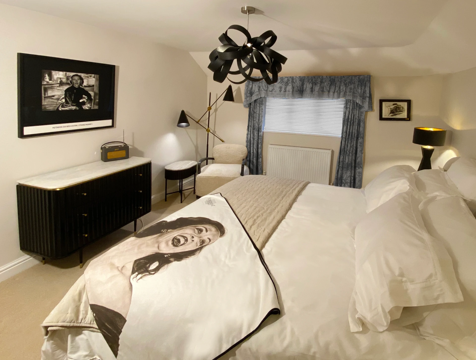 Modern minimalist bedroom in black and white featuring a bed with patterned linens, a fluted black dresser, and four framed pop-art portraits on the wall.